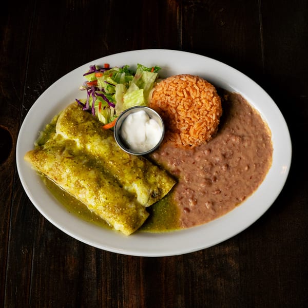 Two green enchiladas with rice, refried beans, a side salad, and sour cream on a white plate.