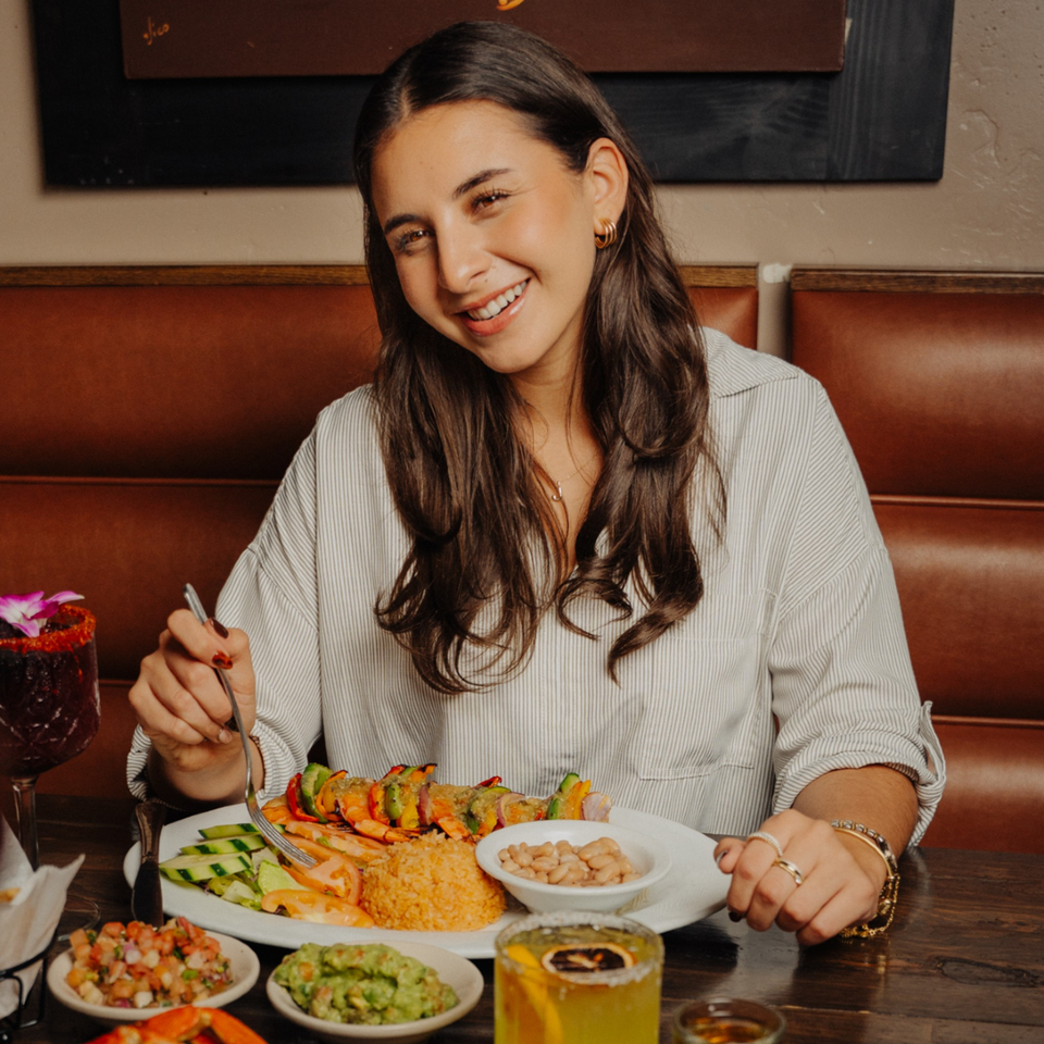 Smiling woman enjoying shrimp skewers, rice, beans, guacamole, and salsa at El Tarasco Restaurant.