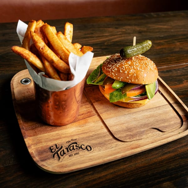 El Tarasco Restaurant's burger with fries, topped with a pickle, on a wooden serving board.
