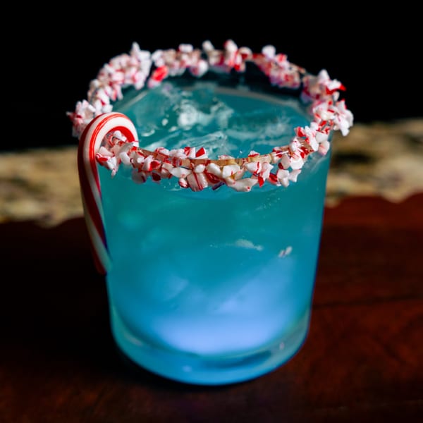 Blue cocktail with a crushed candy cane rim and a whole candy cane garnish.