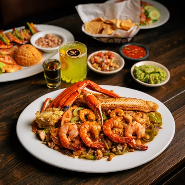 Mexican seafood platter with shrimp, crab, fish, guacamole, salsa, chips, and a margarita.
