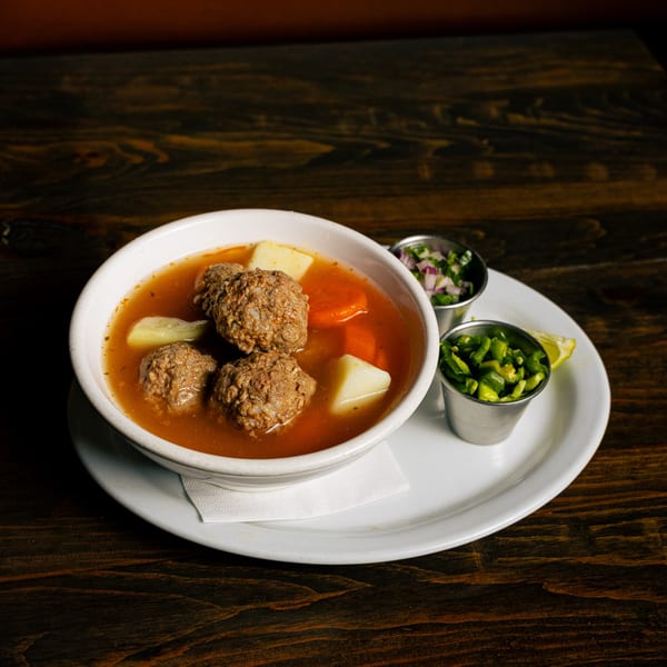 Mexican albondigas soup with meatballs, potatoes, carrots, and sides of chopped onions and jalapeños.