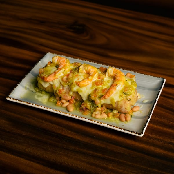 Shrimp and beans covered in melted cheese and green sauce on a rectangular plate.