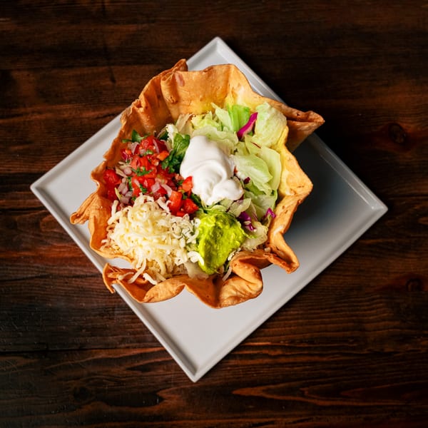 A taco salad in a crispy tortilla bowl with lettuce, pico de gallo, cheese, sour cream, and guacamole.