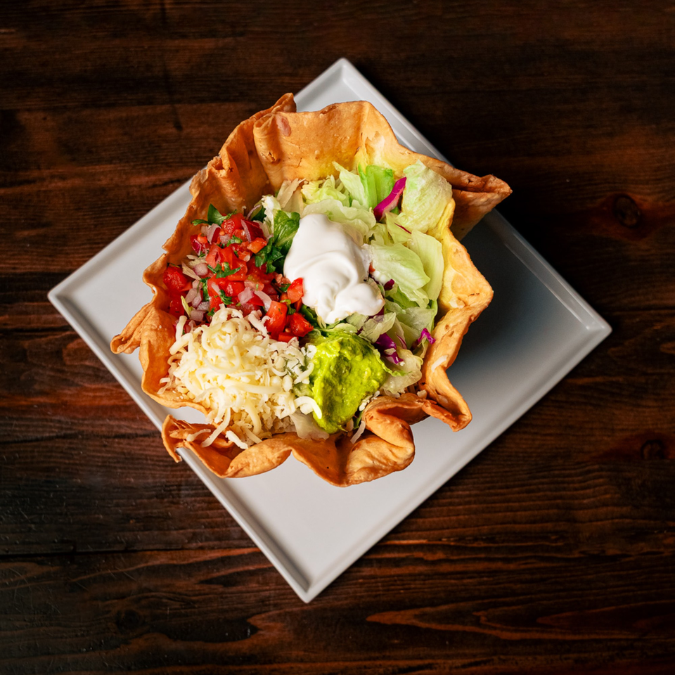 A taco salad in a crispy tortilla bowl with lettuce, pico de gallo, cheese, sour cream, and guacamole.