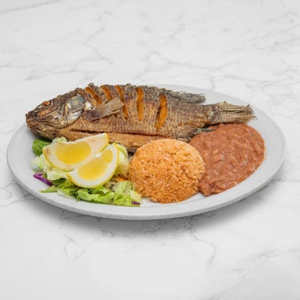 A whole fried fish with rice, refried beans, and a side salad with lemon wedges.