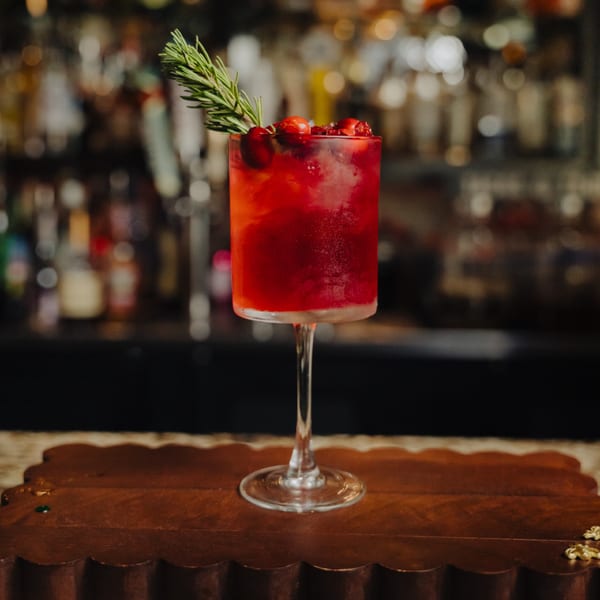 Red cocktail with cranberries and rosemary garnish on a wooden bar top at El Tarasco Restaurant Mooney.
