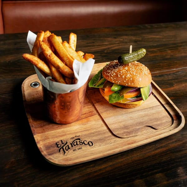 A burger with cheese, lettuce, tomato, onion, and avocado, served with fries on a wooden board.