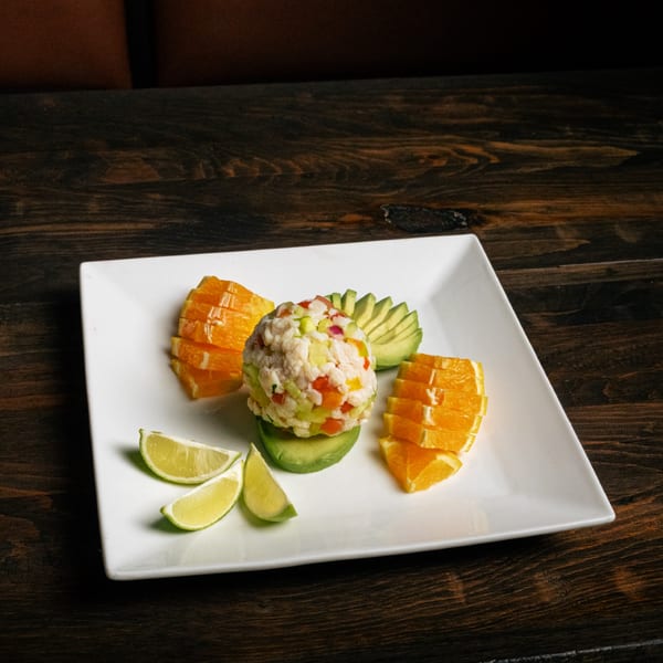 Ceviche with avocado, orange slices, and lime wedges on a white plate at El Tarasco Restaurant Mooney.