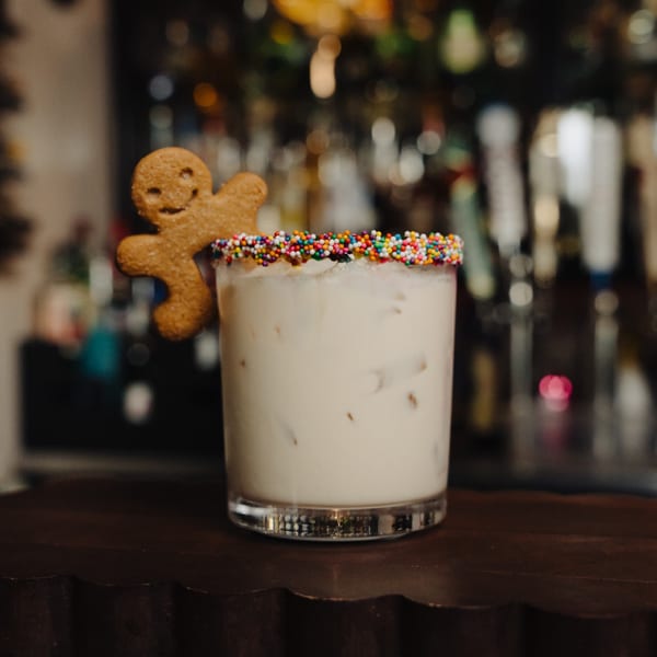 White cocktail with colorful sprinkles on the rim and a gingerbread man cookie garnish.