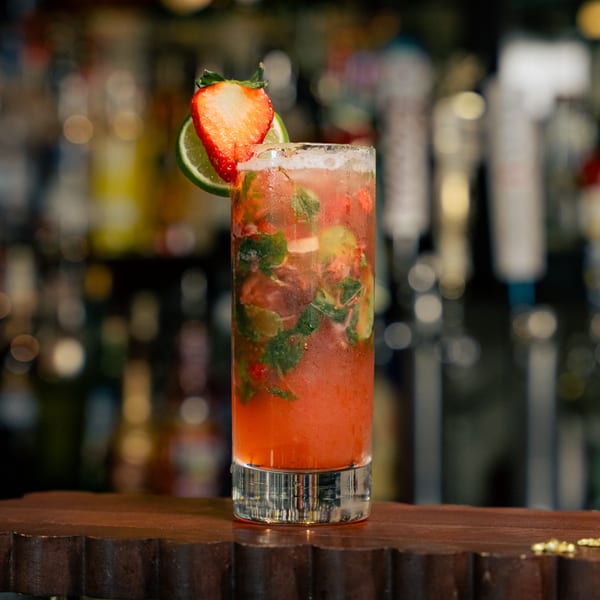Strawberry mojito with lime and mint, garnished with a strawberry slice, on a bar.